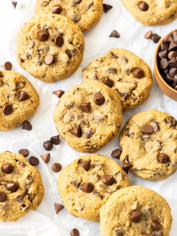 whole wheat chocolate chip cookies on a baking sheet with a small bowl of chocolate chips.