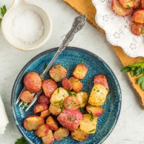 a teal plate with air fryer roasted radishes, fresh radishes, and a small dish of salt.