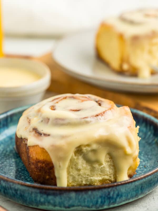 An overnight cinnamon roll on a blue plate with icing dripping down the side.