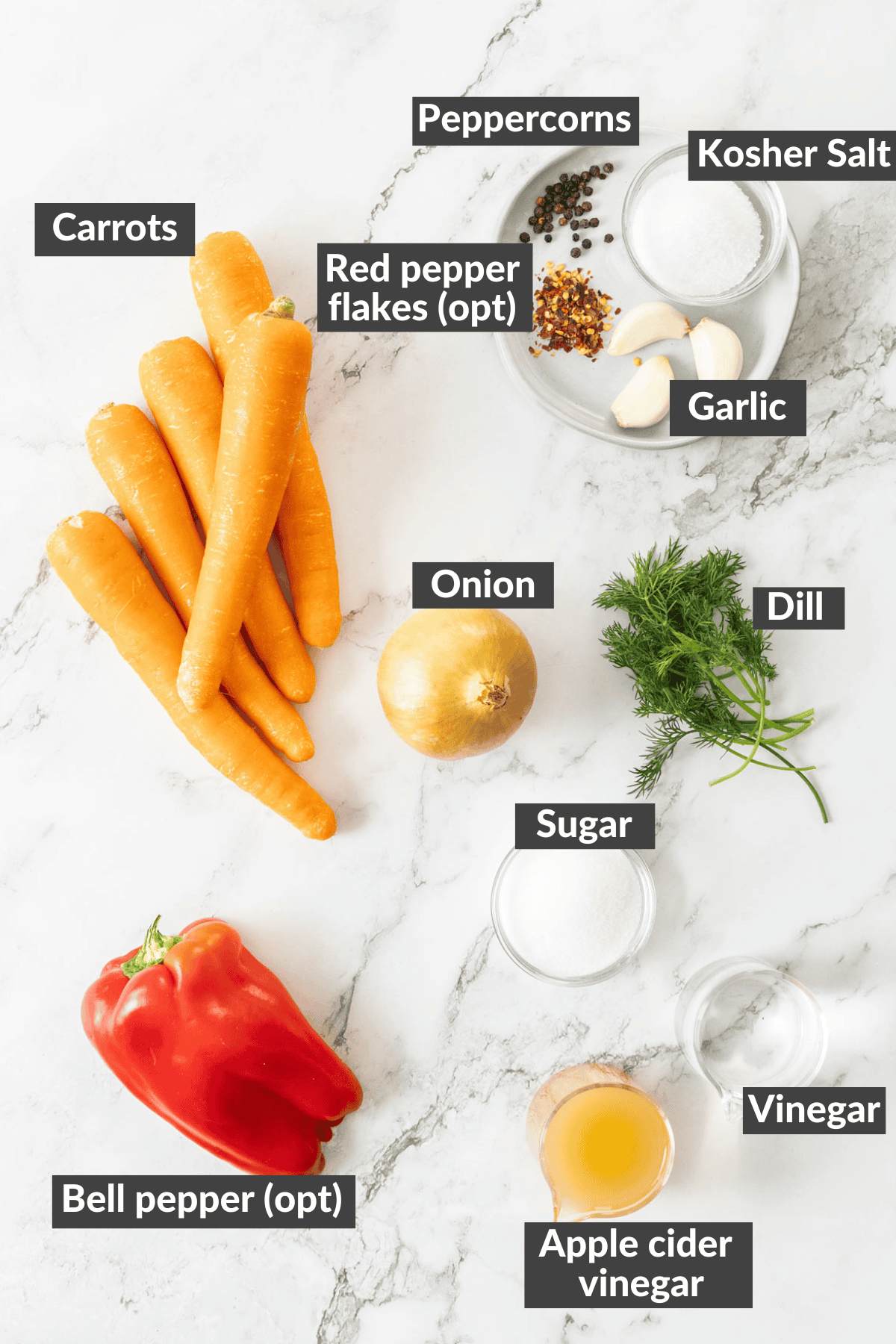Carrots, onions, garlic, dill, and other ingredients on a marbled board.