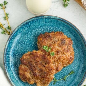 Two breakfast sausage patties on a blue speckled plate with sprigs of fresh thyme.