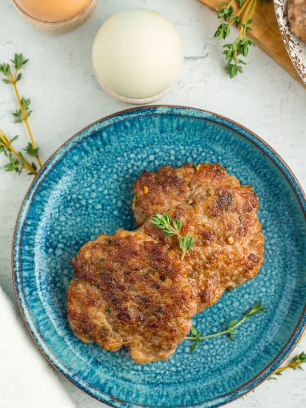 Two breakfast sausage patties on a blue speckled plate with sprigs of fresh thyme.
