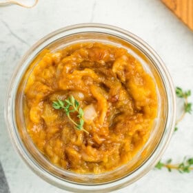 a glass jar of caramelized onions topped with two small sprigs of fresh thyme.