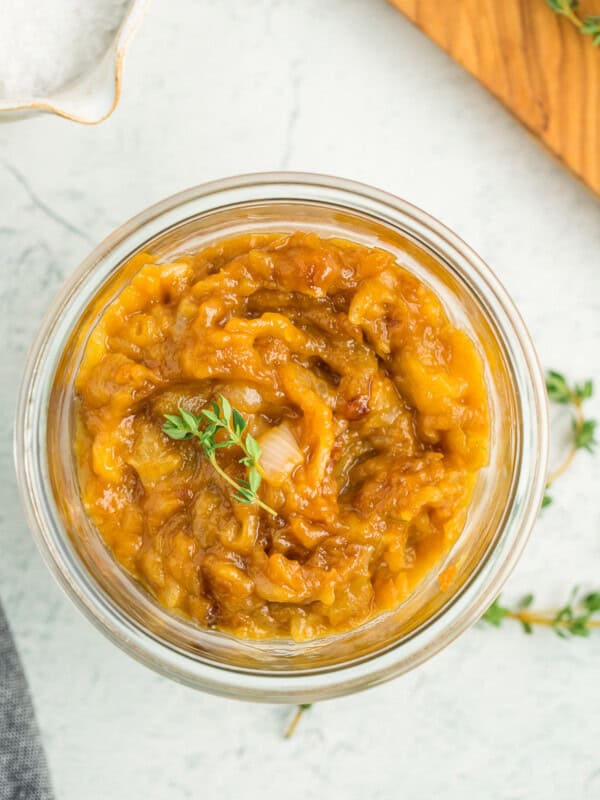 a glass jar of caramelized onions topped with two small sprigs of fresh thyme.