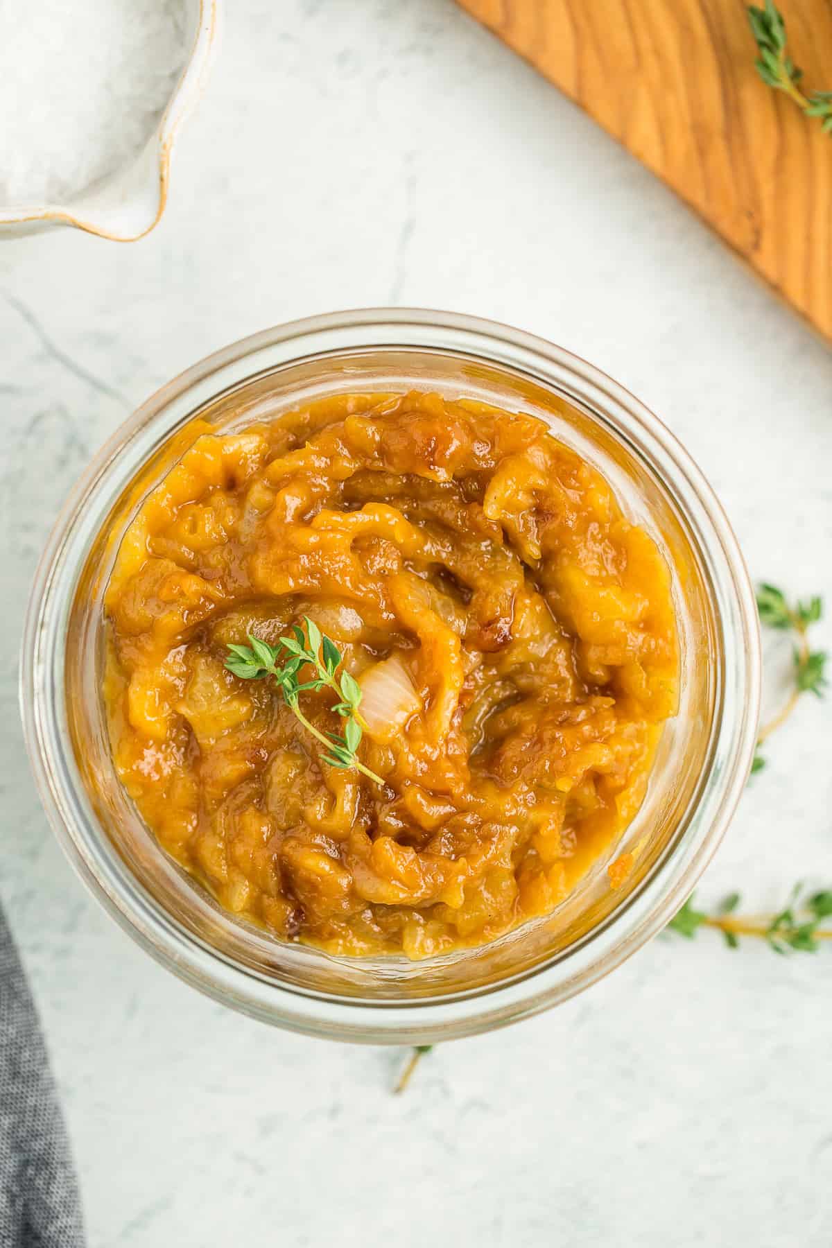 a glass jar of caramelized onions topped with two small sprigs of fresh thyme.