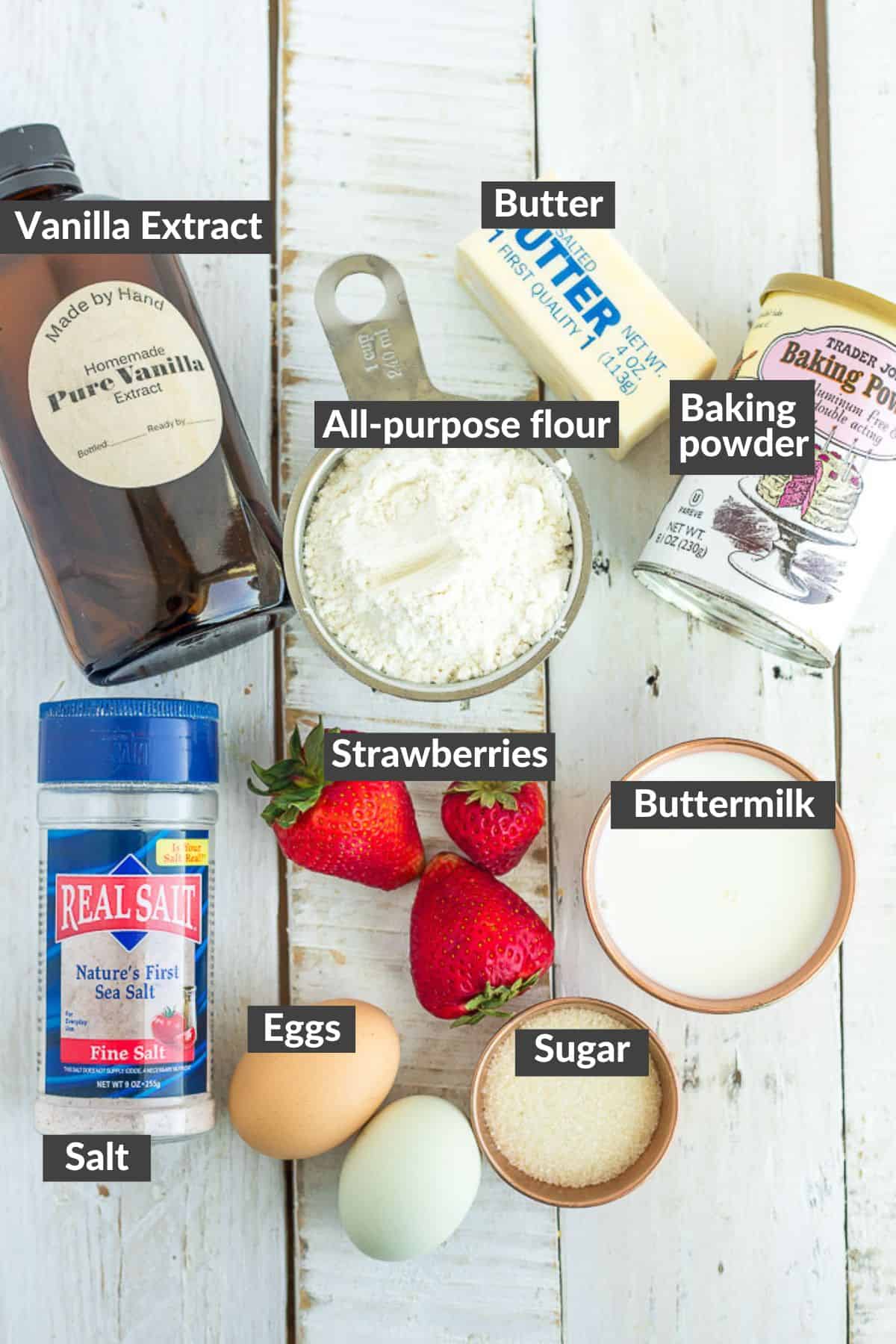eggs, flour, sugar, strawberries, and other ingredients on a white wooden board.