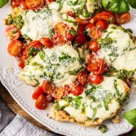 a grey plate with grilled margherita chicken topped with basil and sliced tomatoes.
