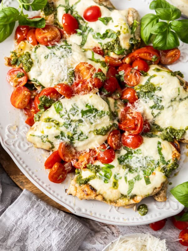 a grey plate with grilled margherita chicken topped with basil and sliced tomatoes.