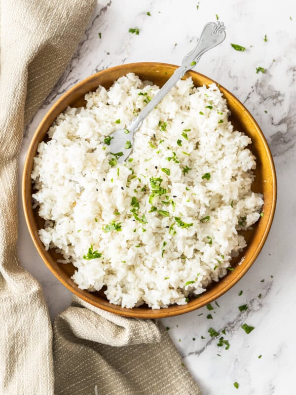 a wooden bowl with Instant Pot coconut rice topped with chopped parsley with a fork in the bowl.