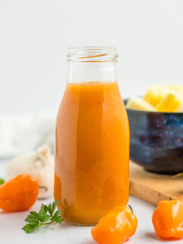 a glass jar of pineapple habanero hot sauce with habaneros on a marbled board.