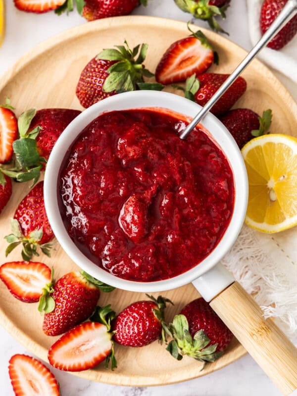 a white saucepan of strawberry compote, with sliced strawberries sprinkled around it.