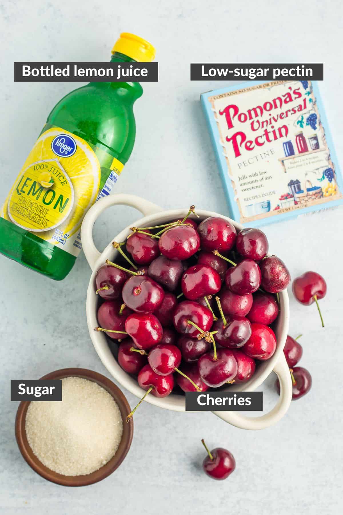 lemon juice, a bowl of sugar, pectin, and a bowl of cherries.