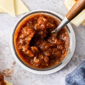 a glass jar of tomato jam with a spoon with a wooden handle.