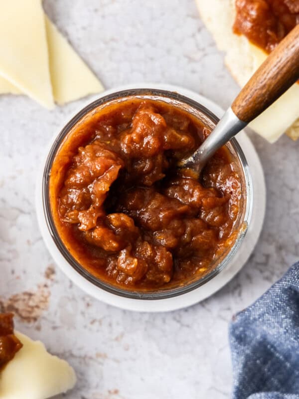 a glass jar of tomato jam with a spoon with a wooden handle.