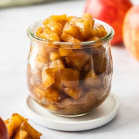 A side profile image of apple compote in a glass jar on a small white plate.