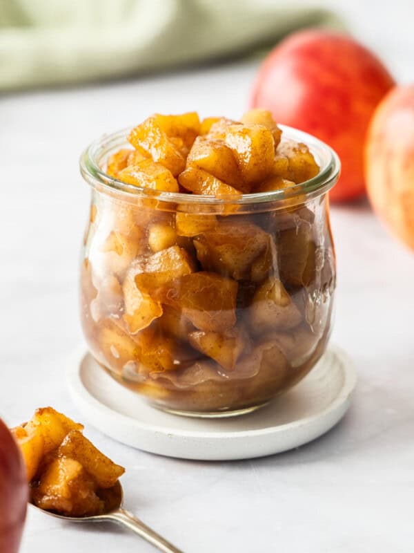 A side profile image of apple compote in a glass jar on a small white plate.