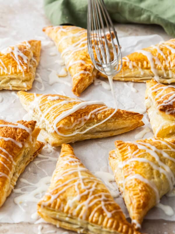 puff pastry apple turnovers with a whisk drizzling glaze over the top.