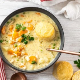 two bowls of chicken pot pie soup topped with biscuits and spoons.