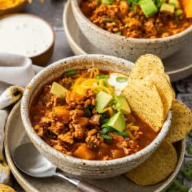 two bowls of chili topped with chips, sour cream, cheese, avocado, and green onions.