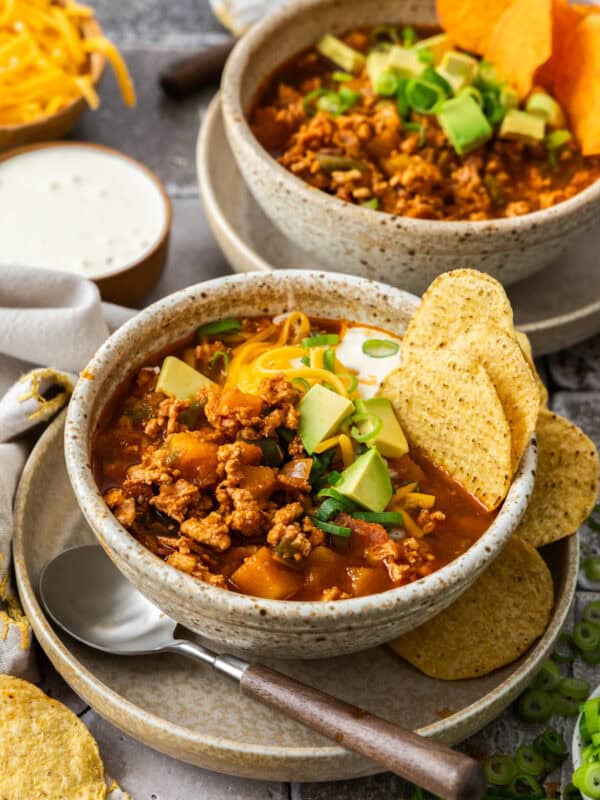 two bowls of chili topped with chips, sour cream, cheese, avocado, and green onions.