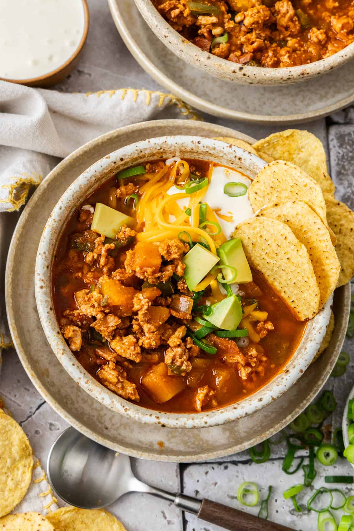 A bowl of chili with various toppings and corn chips on the side.