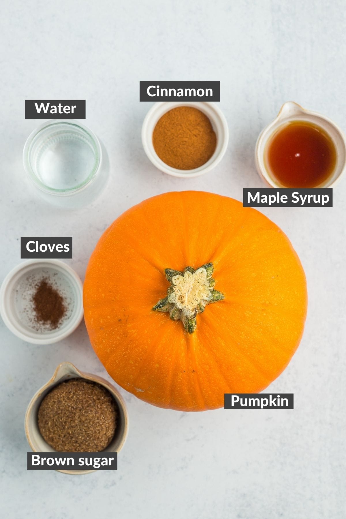 pumpkin, cinnamon, maple syrup, brown sugar, cloves, and water on a grey board.