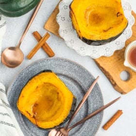 Two plates with acorn squash halves, silverware, salt, and cinnamon sticks.
