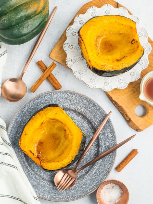 Two plates with acorn squash halves, silverware, salt, and cinnamon sticks.