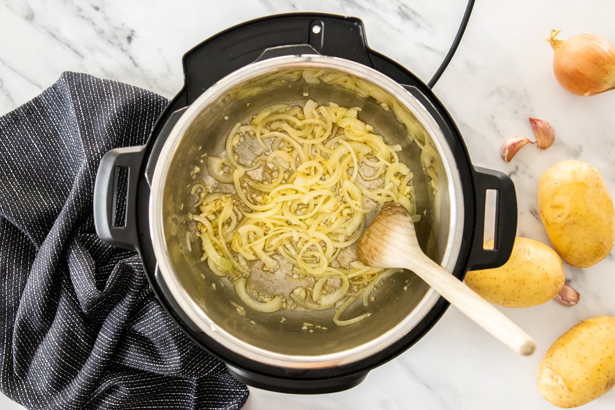 onions and a wooden spoon in an Instant Pot.