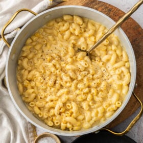 a pot with butternut squash macaroni and cheese, a gold spoon, and black pepper.