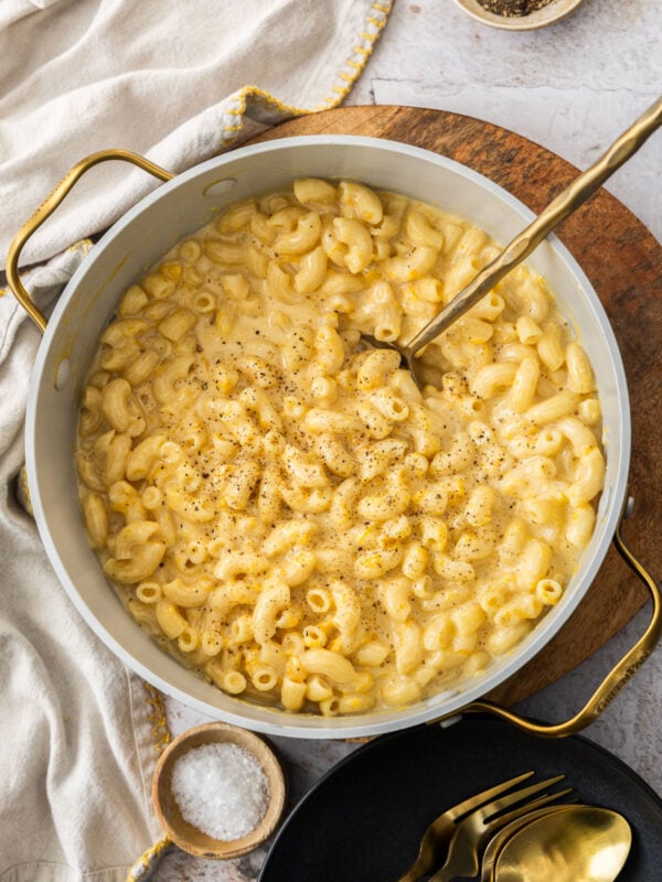 a pot with butternut squash macaroni and cheese, a gold spoon, and black pepper.