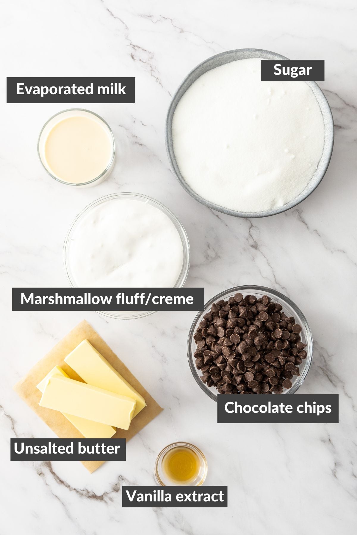 evaporated milk, sugar, marshmallow fluff, chocolate chips, butter, and vanilla extract on a marbled board.