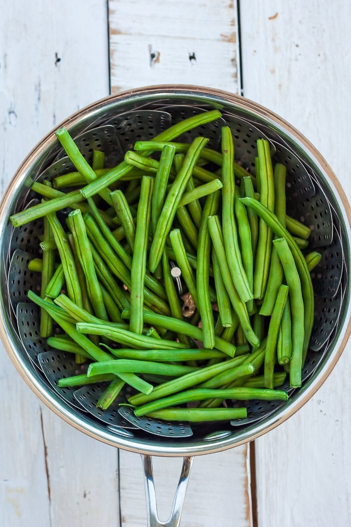 green beans in a steamer basket in a saucepan.