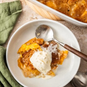 a white plate with a serving of peach cobbler topped with vanilla ice cream.