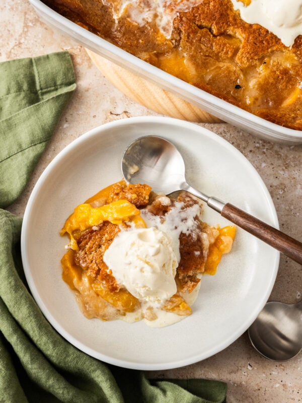 a white plate with a serving of peach cobbler topped with vanilla ice cream.