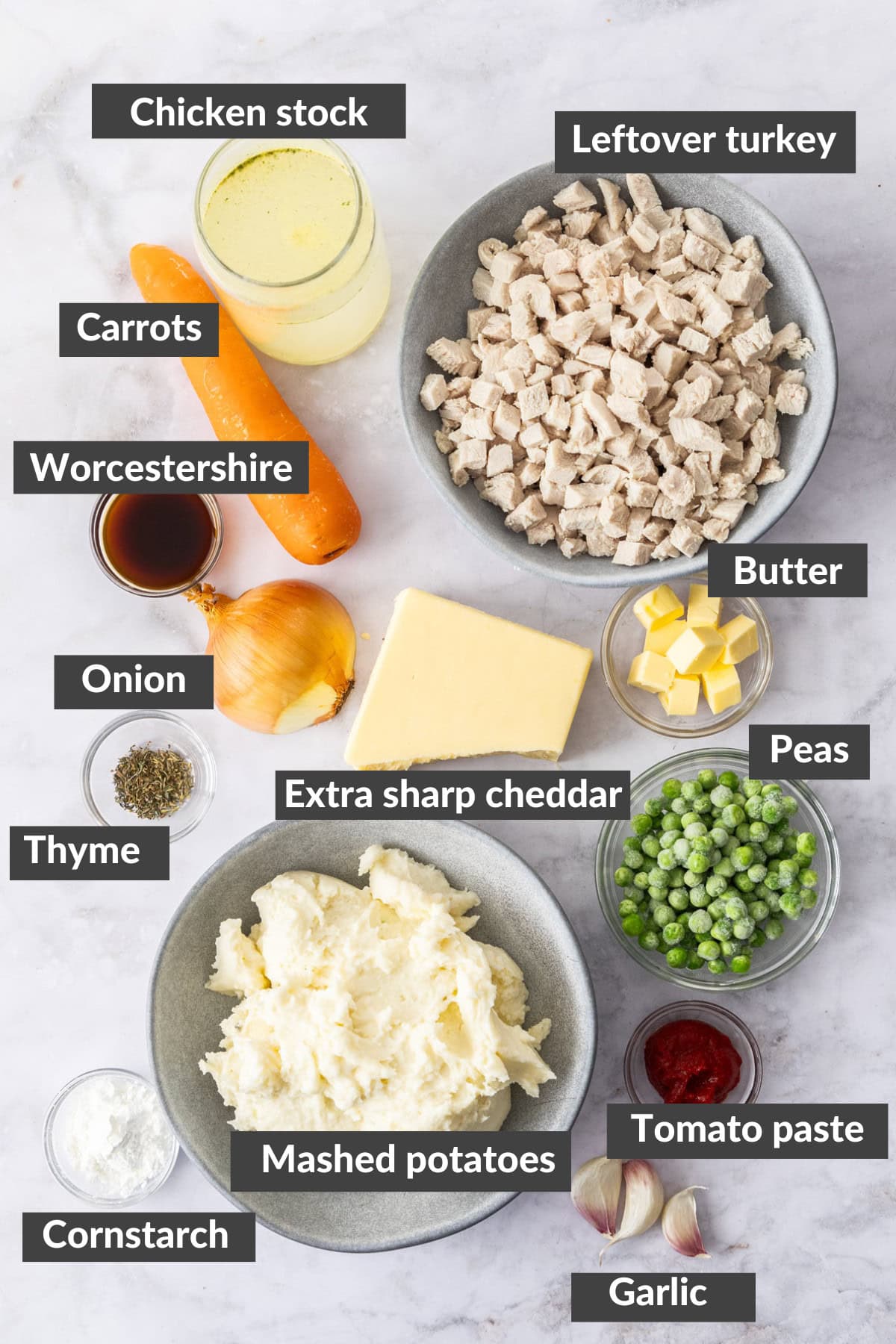 bowls of peas, mashed potatoes, diced turkey, and other ingredients on a marble board.