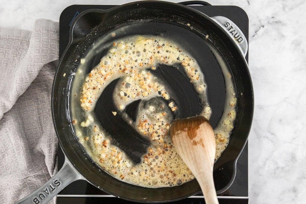 a black cast iron skillet with butter, onions, and garlic being cooked.