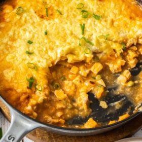 a cast iron skillet of a mashed potato topped casserole with a scoop missing.