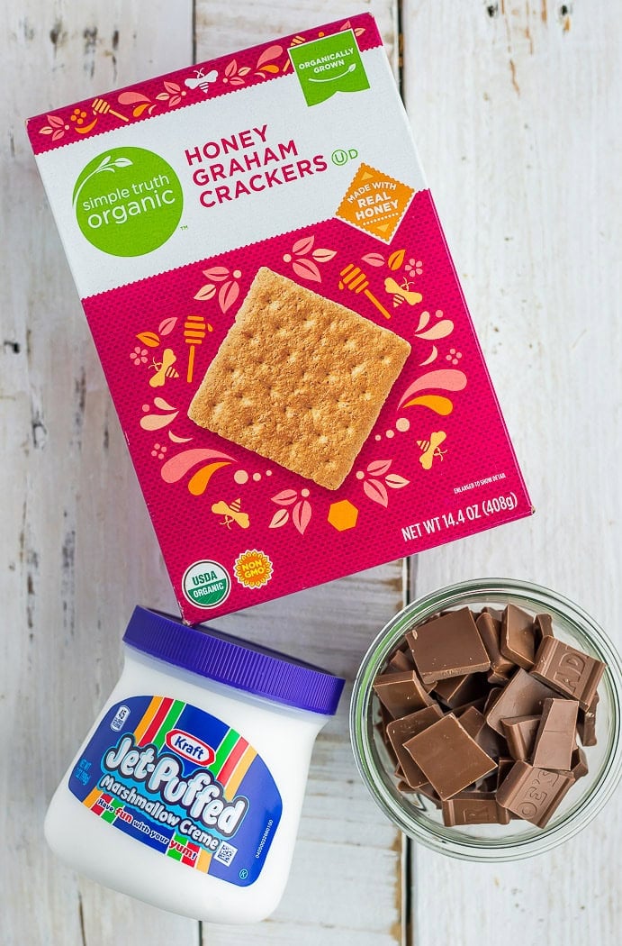 a box of graham crackers, a jar of marshmallow creme, and pieces of chocolate in a bowl.