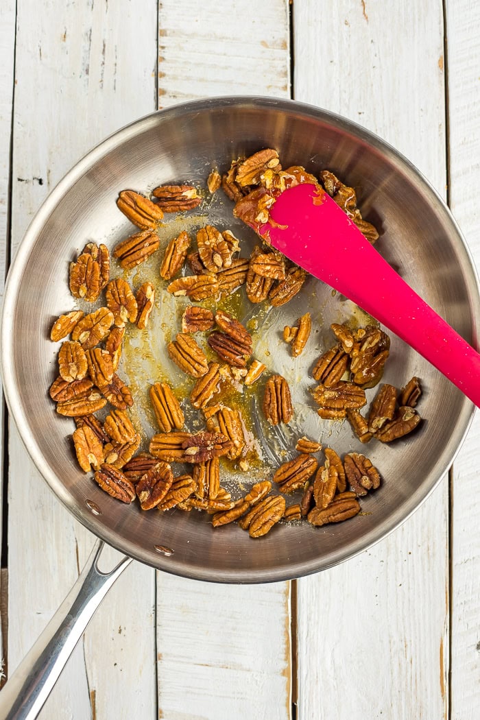 pecans and a red spatulat in a skillet.