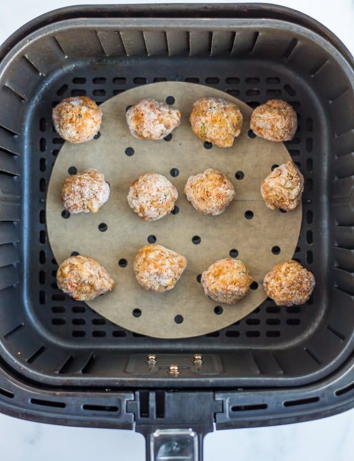 uncooked crab cakes in an air fryer basket.