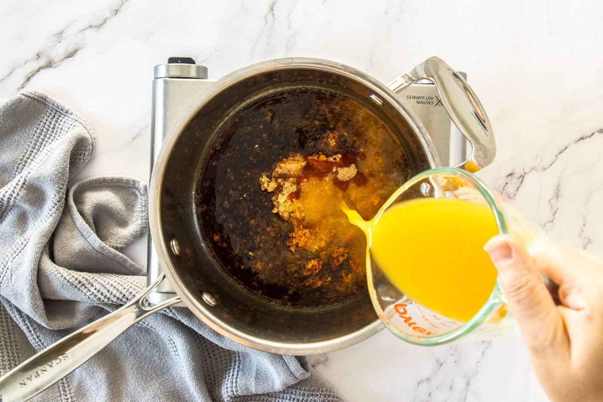 orange juice being poured into a saucepan on a burner.