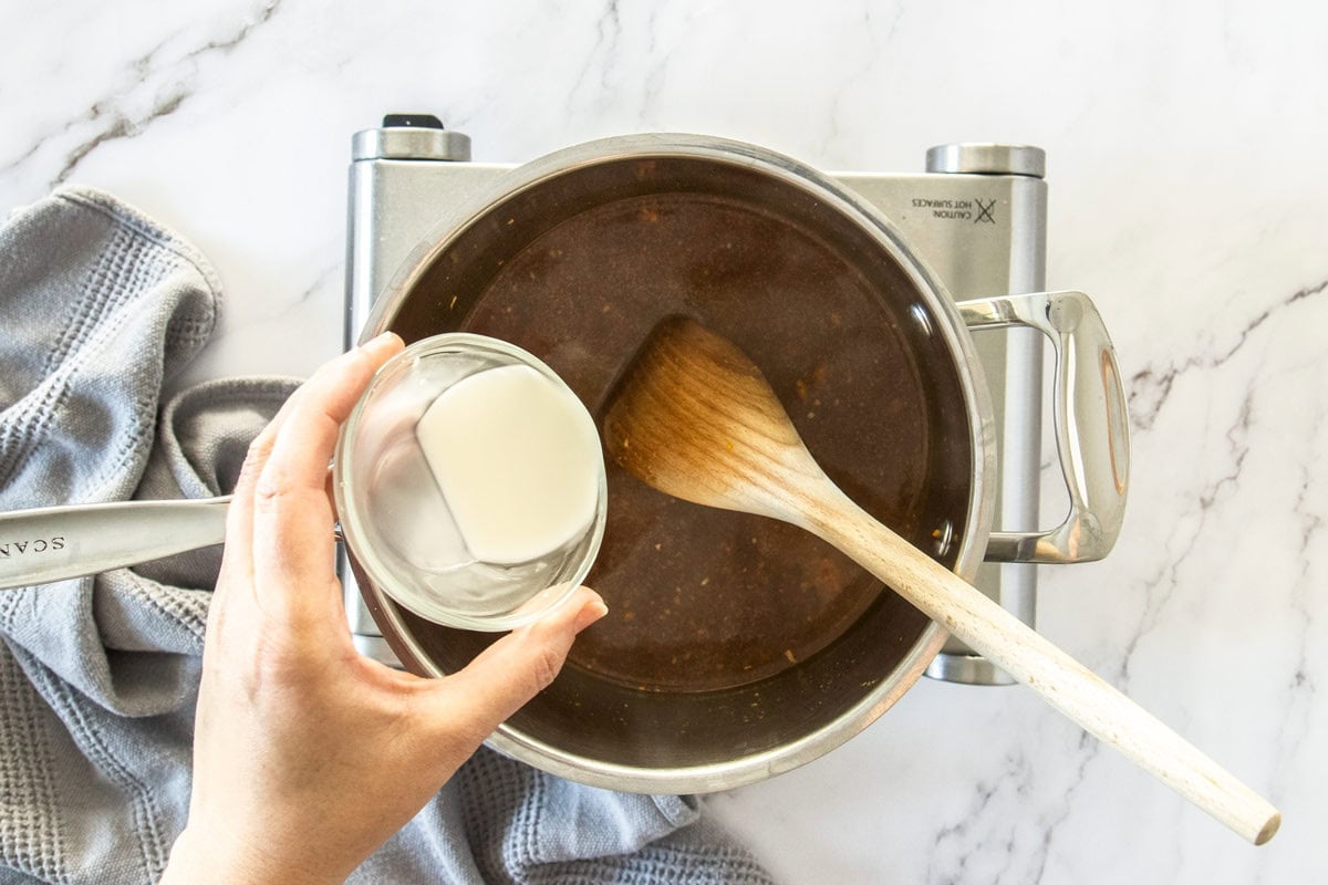 a saucepan on a burner with a spoon in it and a small bowl of cornstarch.
