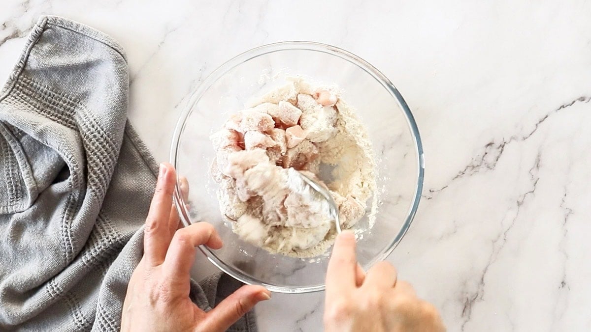 a hand stirring pieces of chicken in a glass bowl.