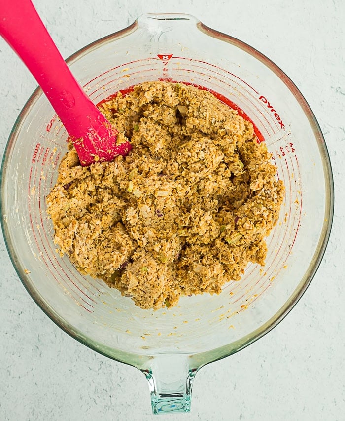 a mixture of salmon cakes in a glass bowl with a red spatula.
