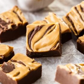 squares of chocolate peanut butter fudge on parchment paper with a small white bowl of peanut butter.
