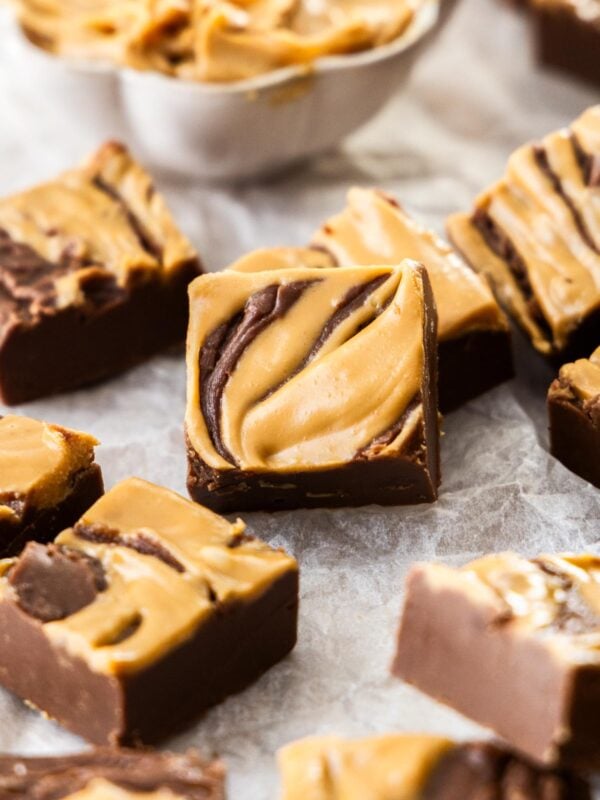 squares of chocolate peanut butter fudge on parchment paper with a small white bowl of peanut butter.