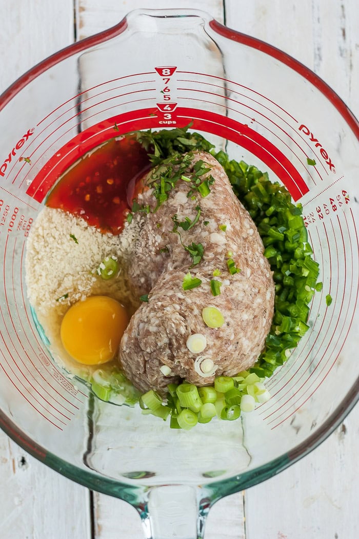 pork, green onions, cilantro, an egg, and other ingredients in a glass bowl.