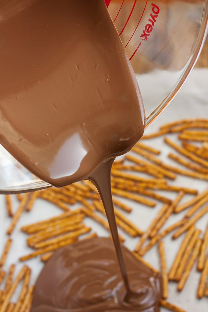 chocolate being poured over a tray of pretzel sticks.
