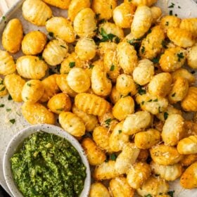 a grey dish with crispy air fryer gnocchi topped with chopped parsley. There are bowls of pesto and marinara.